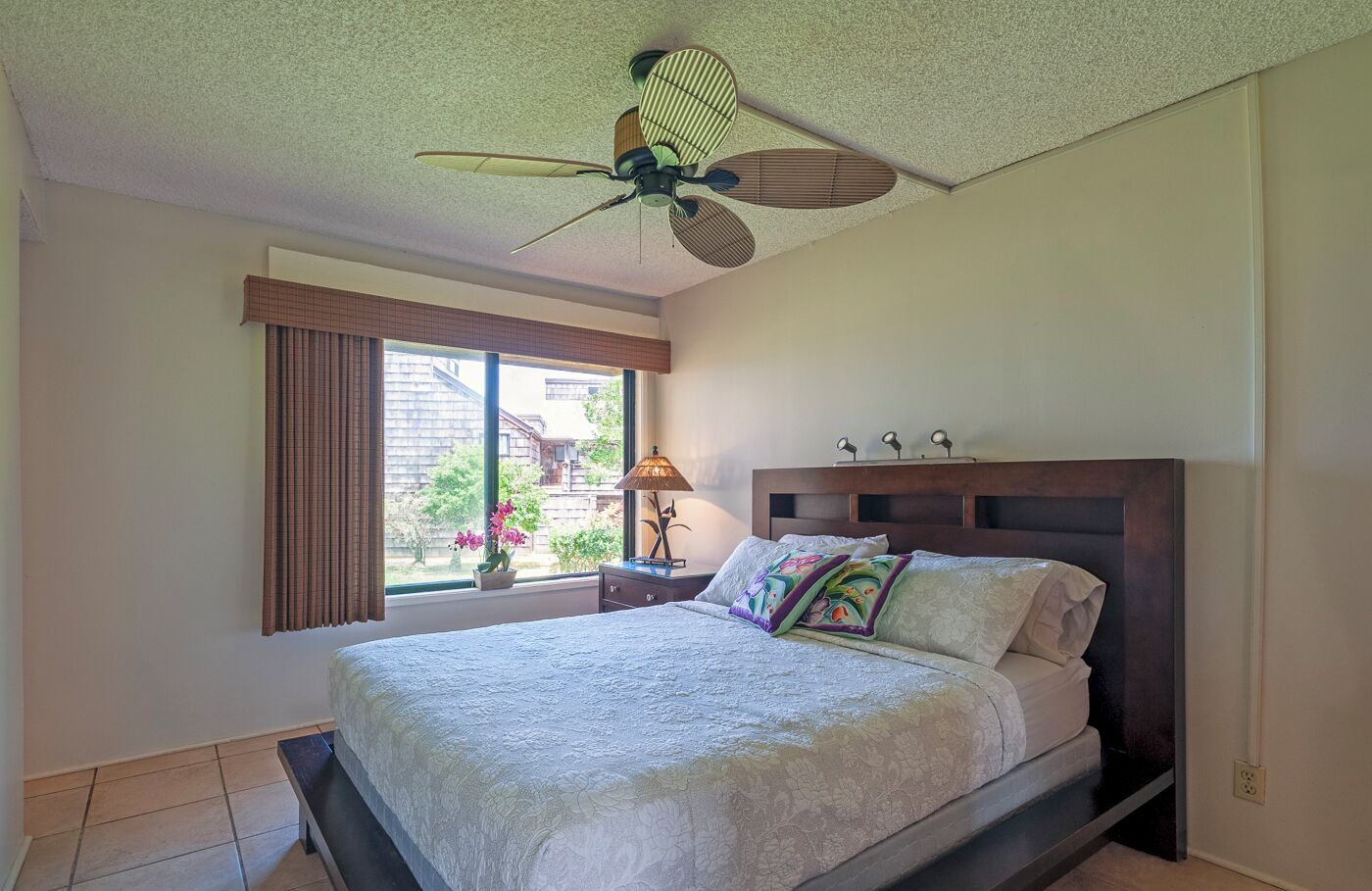 Ein Schlafzimmer mit einem Bett, einem Deckenventilator, einem Fenster mit Vorhängen und Blick ins Freie.