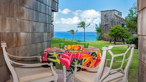 A patio with a table set for two, overlooking a scenic view of the ocean and a building in the background. - Sealodge F1 (Princeville)
