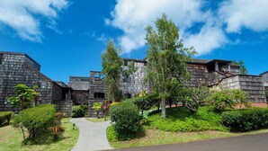 A modern building with a mix of wooden and metal exterior, surrounded by lush greenery and a clear blue sky. - Sealodge F1 (Princeville)