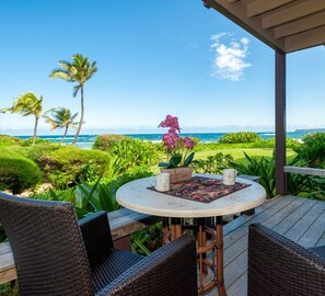 A covered outdoor seating area with wicker chairs, a round table with a floral table runner, and a potted orchid. - Hanalei Colony Resort I-2 (Hanalei)