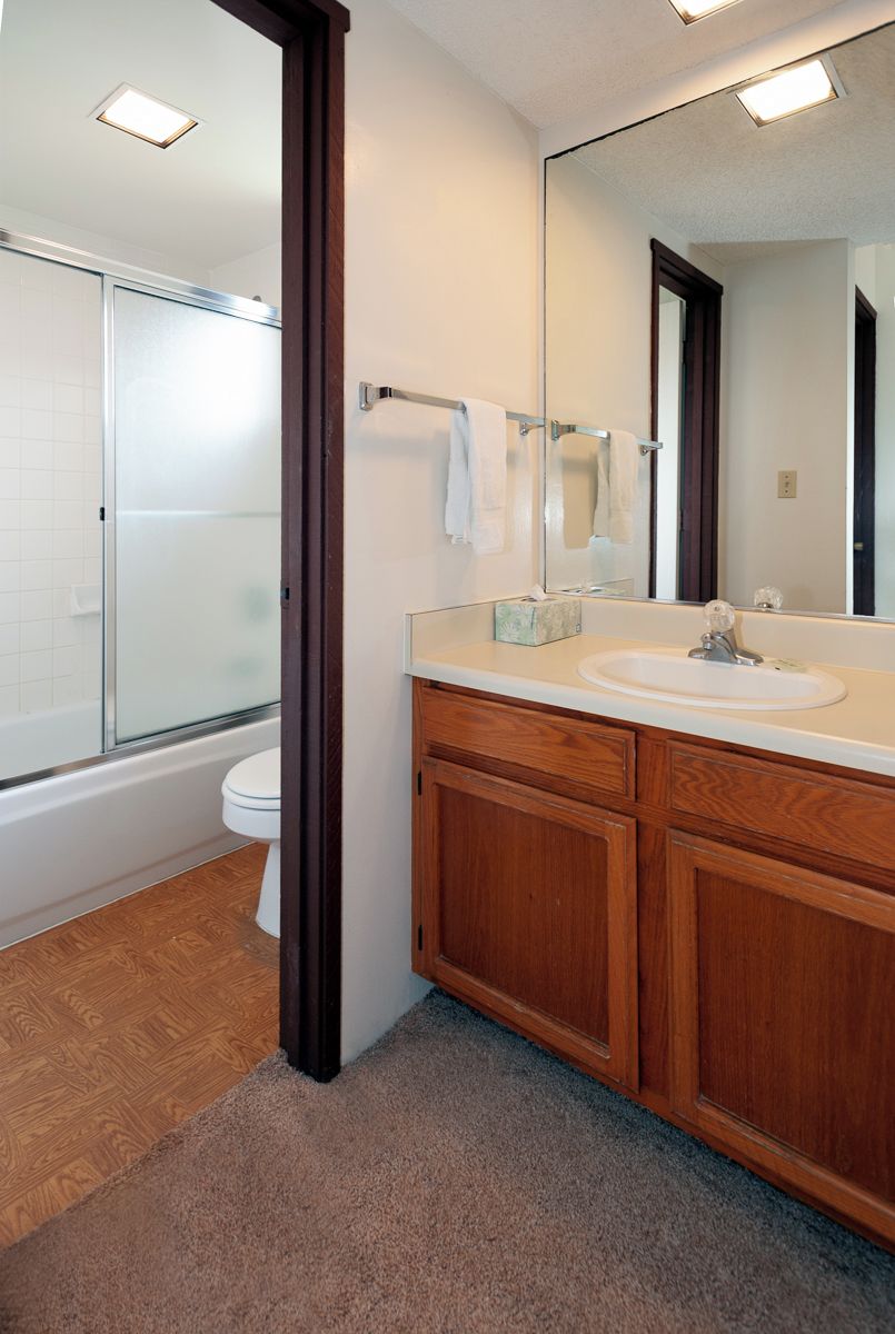 A modern bathroom with a wooden vanity, a large mirror, and a glass shower enclosure.