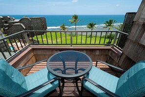 A balcony with a glass table and chairs, overlooking a grassy area and the ocean. - Sealodge F9 (Princeville)