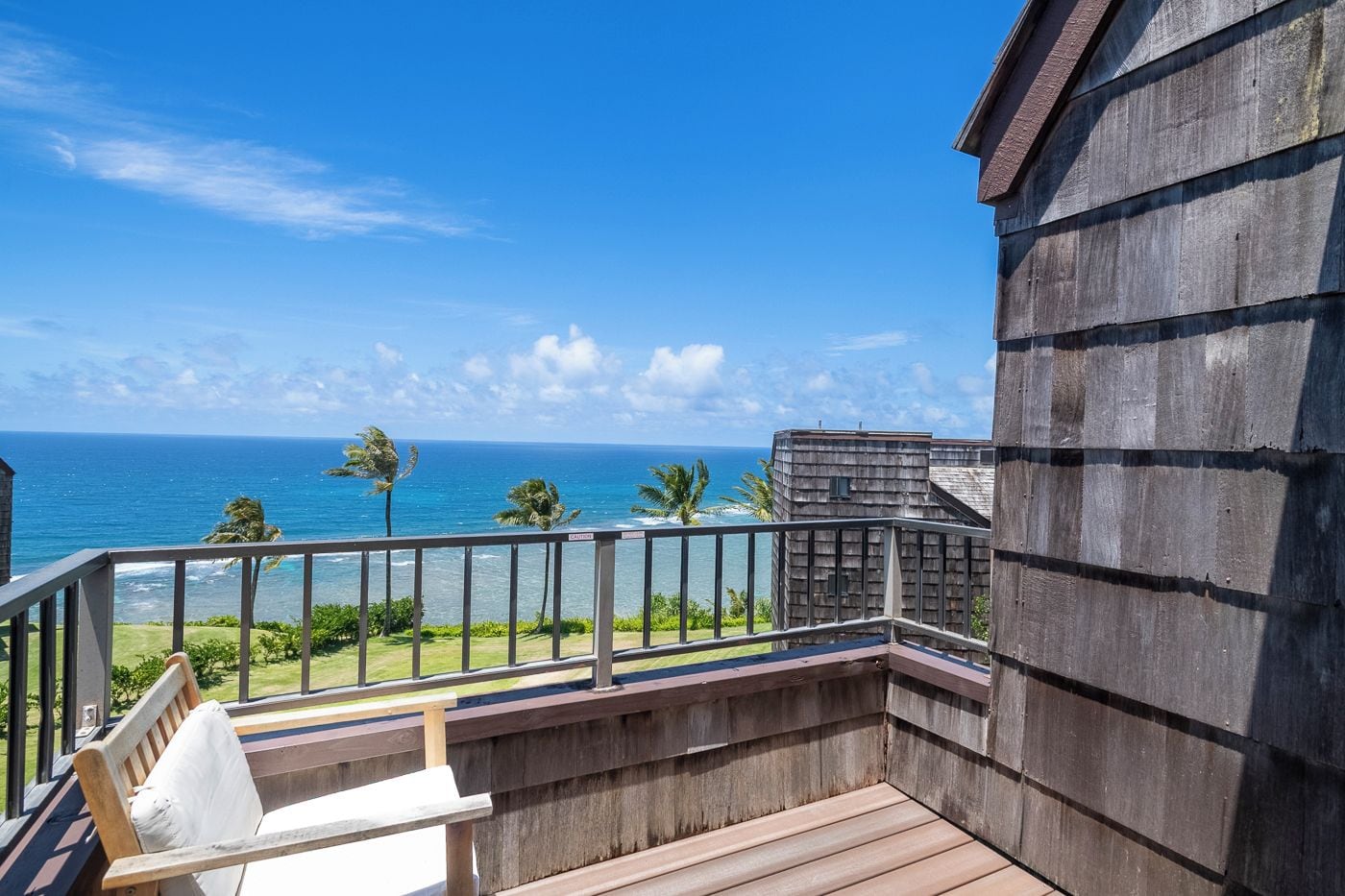 A balcony with a view of the ocean, a wooden deck, and a building with a sloped roof.