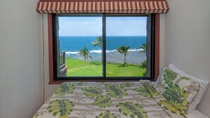Ein Schlafzimmer mit großem Fenster mit Blick aufs Meer, einem Bett mit blattgemustertem Überwurf und einer gestreiften Fensterbank.