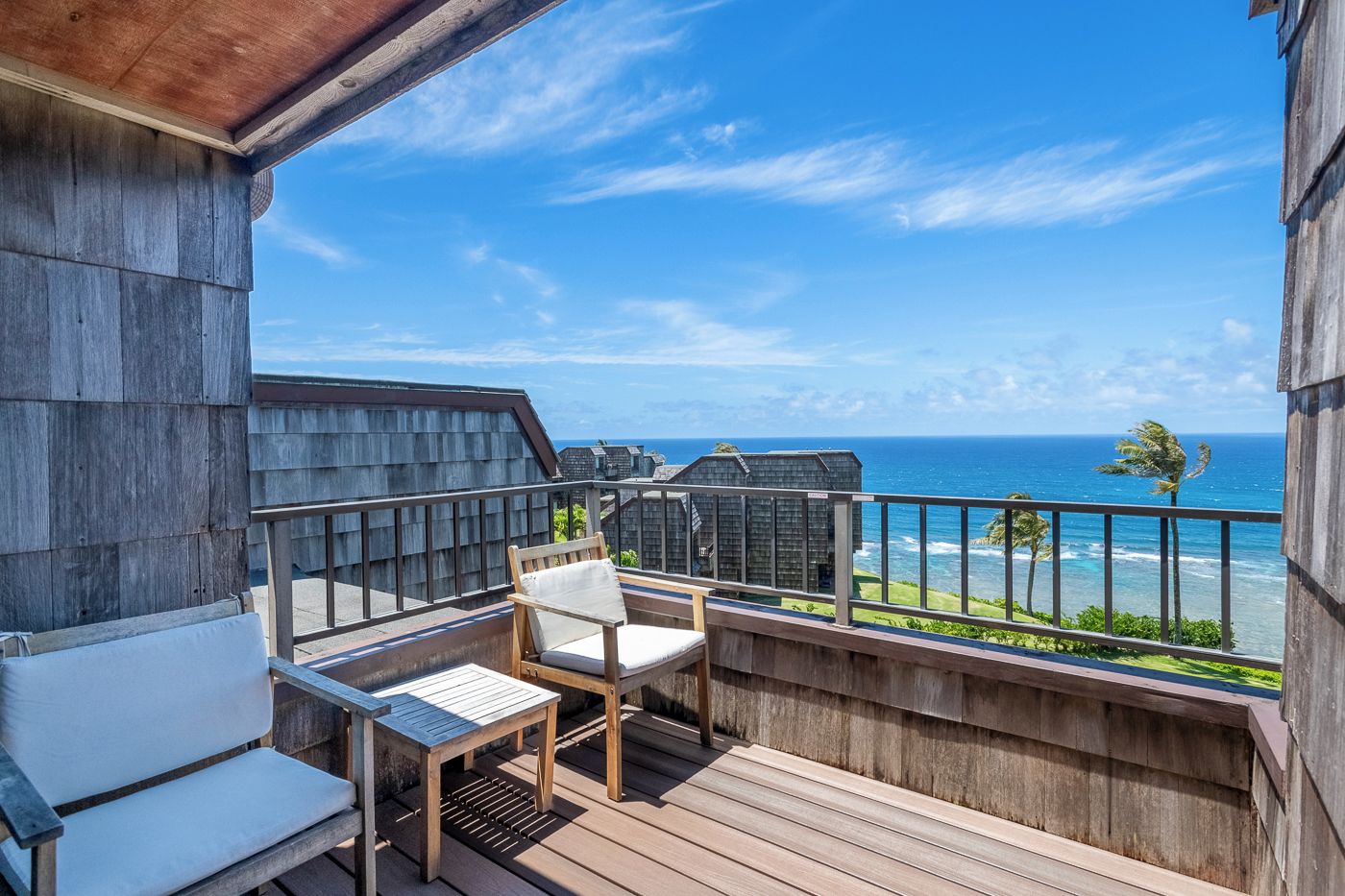A wooden deck with a table and chairs, overlooking a beach and ocean.