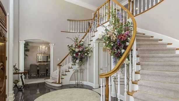 Una imponente escalera con diseño curvo, flanqueada por balaustradas blancas y barandillas de madera.