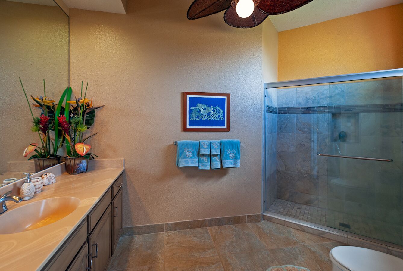 A bathroom with a glass shower, a sink with a mirror, and a wall-mounted towel rack with blue towels.