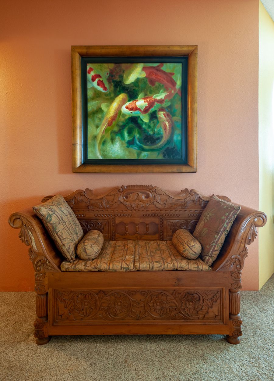 A wooden sofa with intricate carvings and floral-patterned cushions against a peach-colored wall.