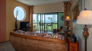 A room with a wicker sofa, a television, a lamp, and a view of a balcony with outdoor furniture.