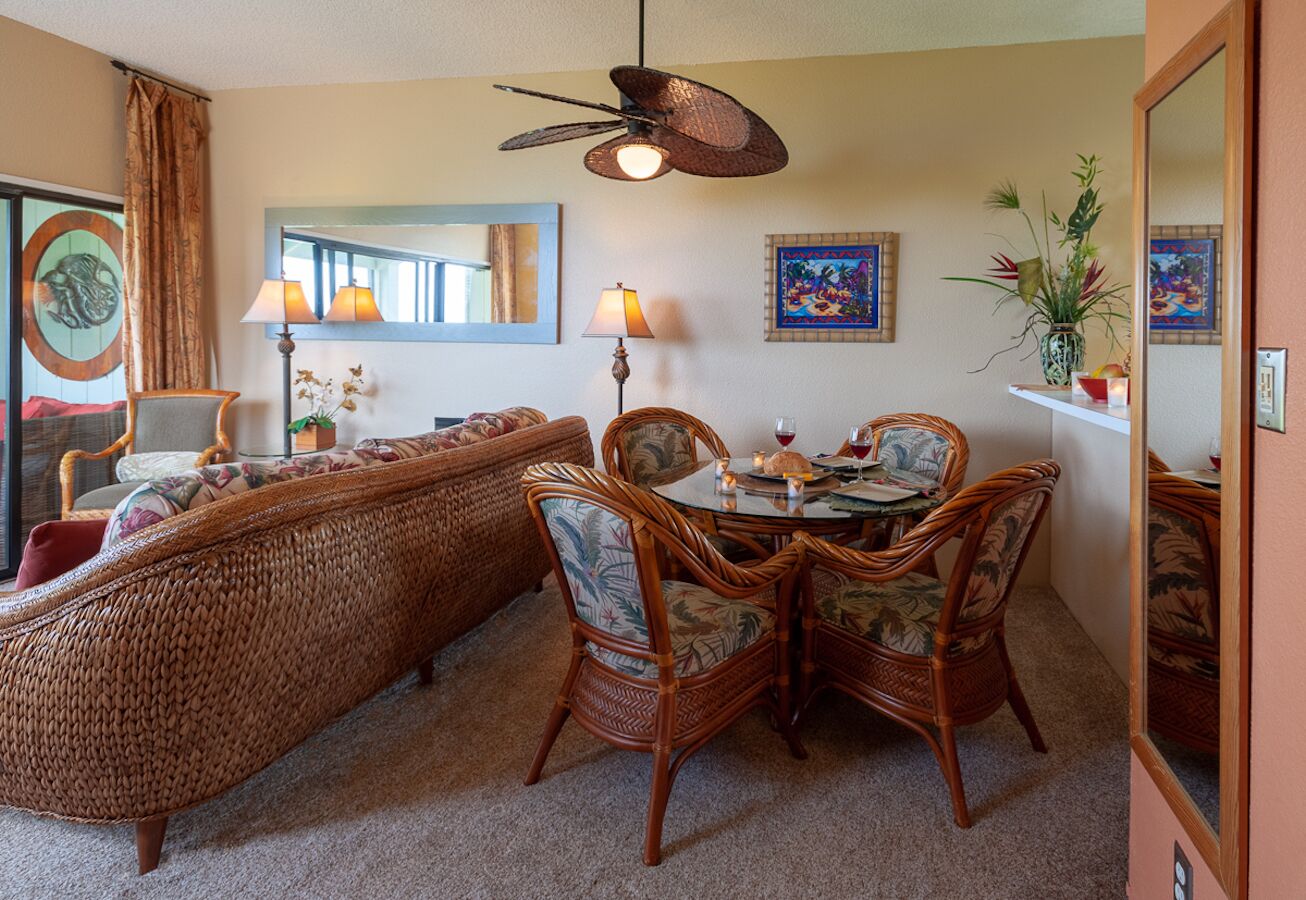 A room with a wicker sofa, wicker dining chairs, a ceiling fan, and a dining table with candles.