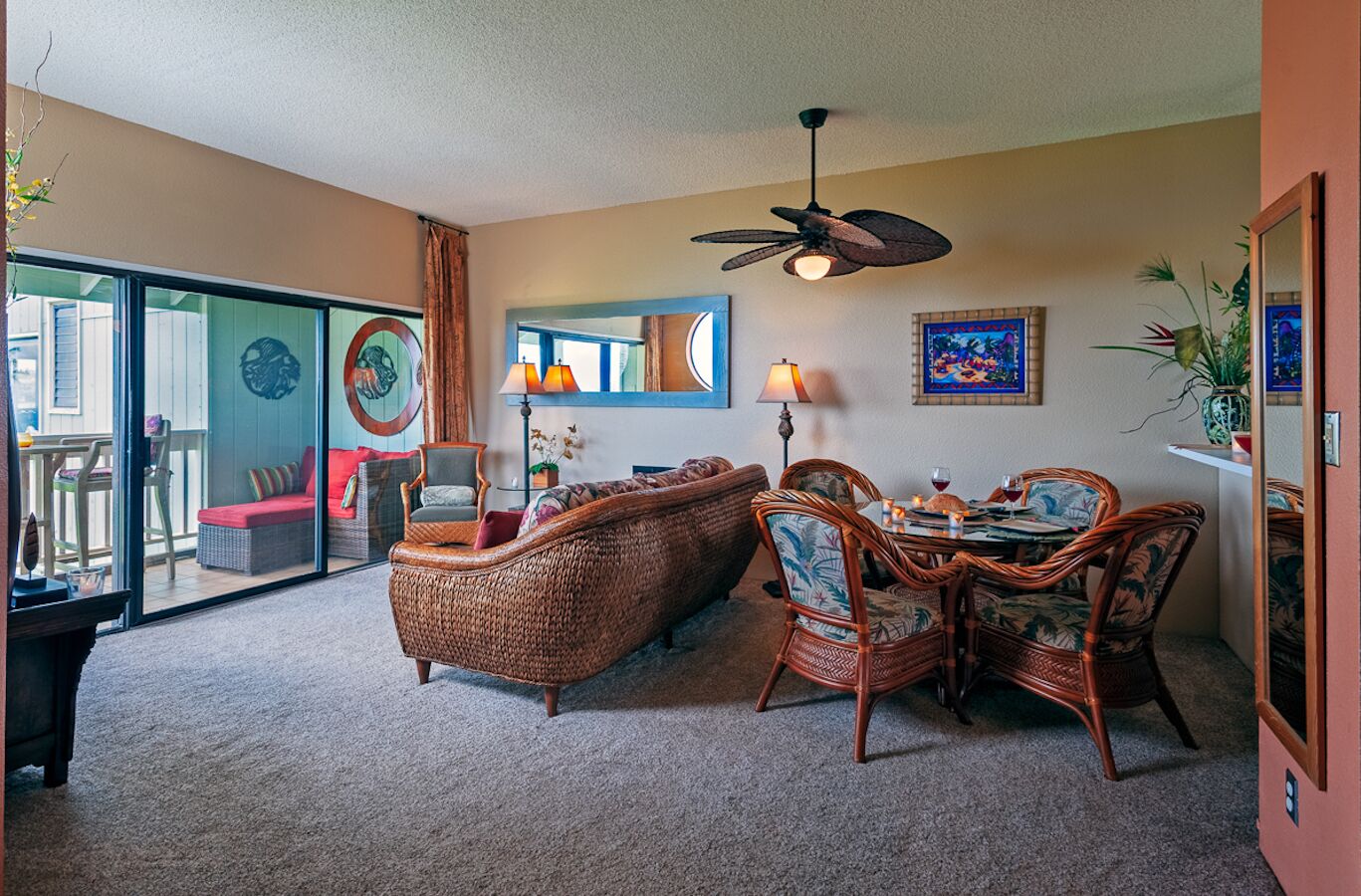 A living room with a wicker sofa, dining table, chairs, a ceiling fan, and a large window.