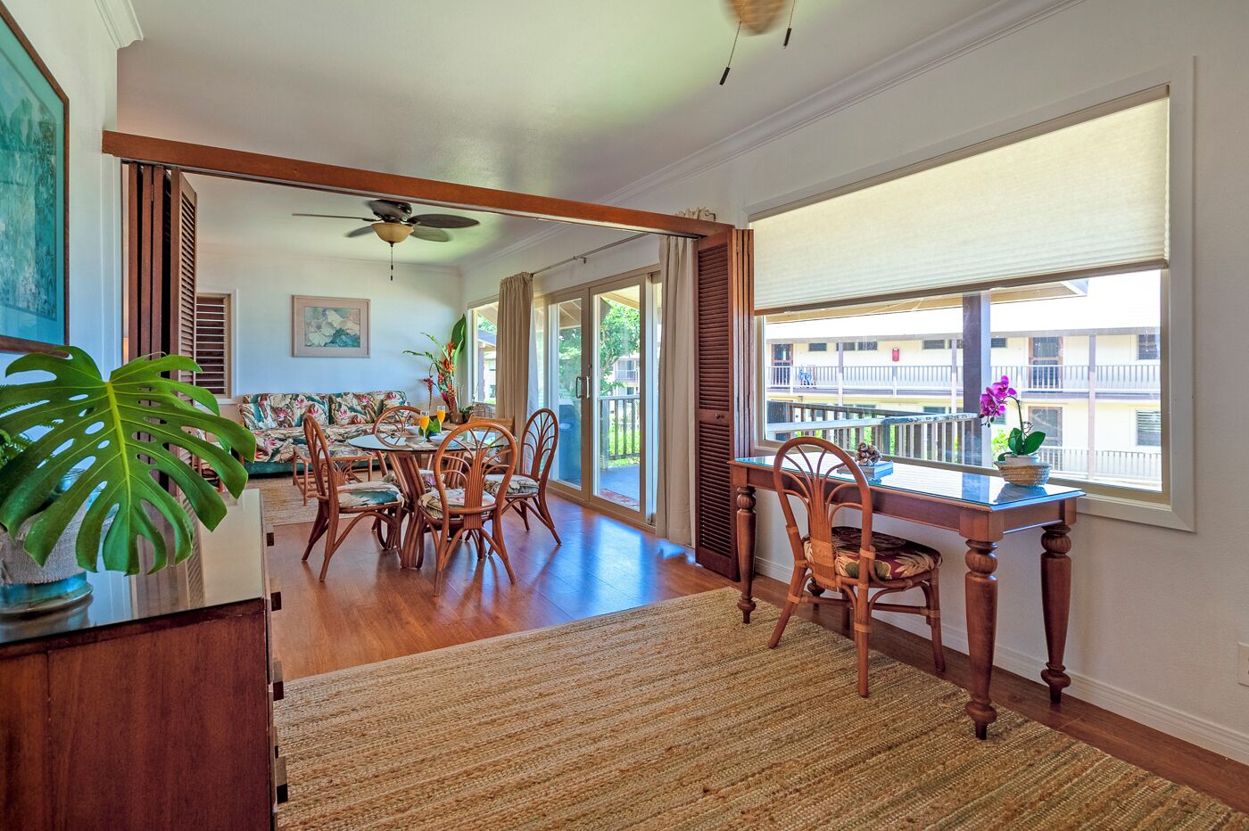 Un comedor espacioso con una mesa y sillas de madera, ventilador de techo y ventanas amplias con vistas al exterior.