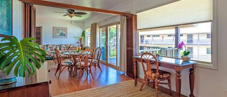 Un comedor espacioso con una mesa y sillas de madera, ventilador de techo y ventanas amplias con vistas al exterior.