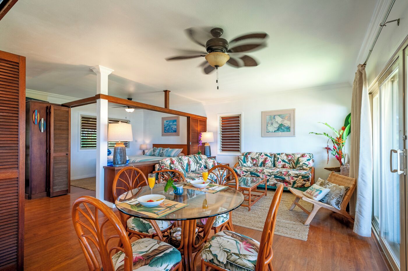 A dining area with a round glass table, wooden chairs, and a ceiling fan.