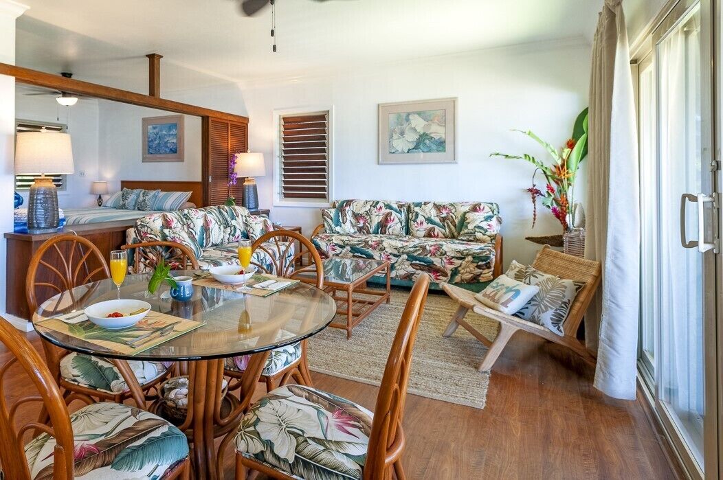 Un salon chaleureux avec une table ronde en verre, des canapés à motifs floraux, des chaises en bois et un coin repas avec une table en verre.