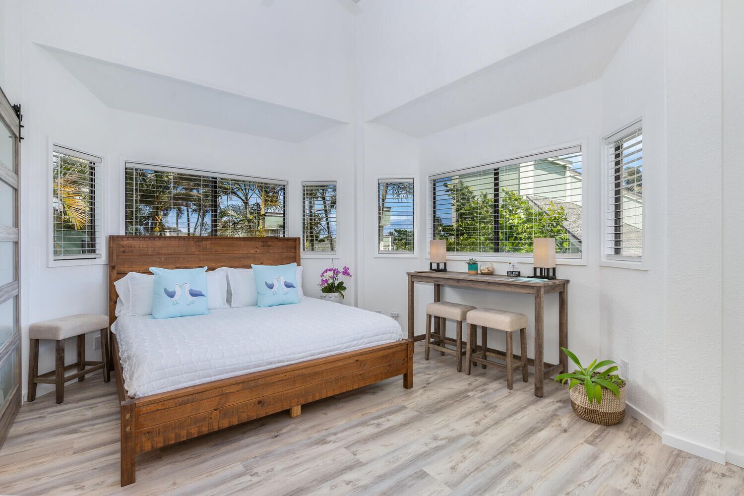 Un dormitorio con una cama de madera, un escritorio con dos sillas y ventanas grandes con persianas.