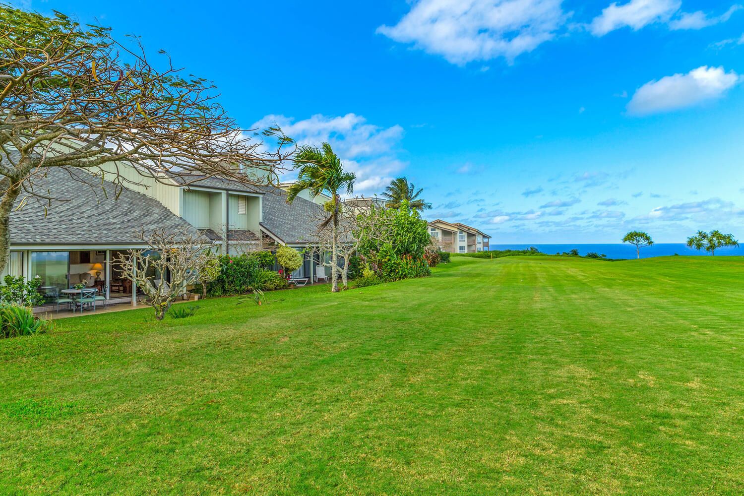 A residential property with a well-maintained lawn, a patio with outdoor furniture, and a view of the ocean.