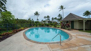 Una piscina con una escalera metálica, rodeada por un deck de hormigón y palmeras.