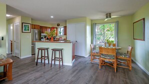 Una cocina espaciosa con una isla central, taburetes de madera y un comedor con sillas de mimbre.