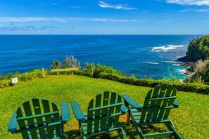 A grassy area with three green Adirondack chairs facing a scenic ocean view. - Alii Kai 1201 (Princeville)