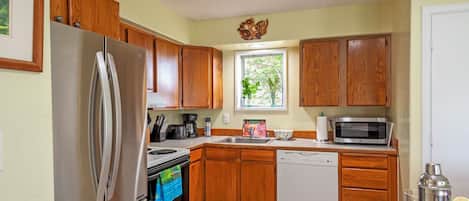 A compact kitchen with wooden cabinets, a stainless steel refrigerator, a microwave, and a dishwasher.