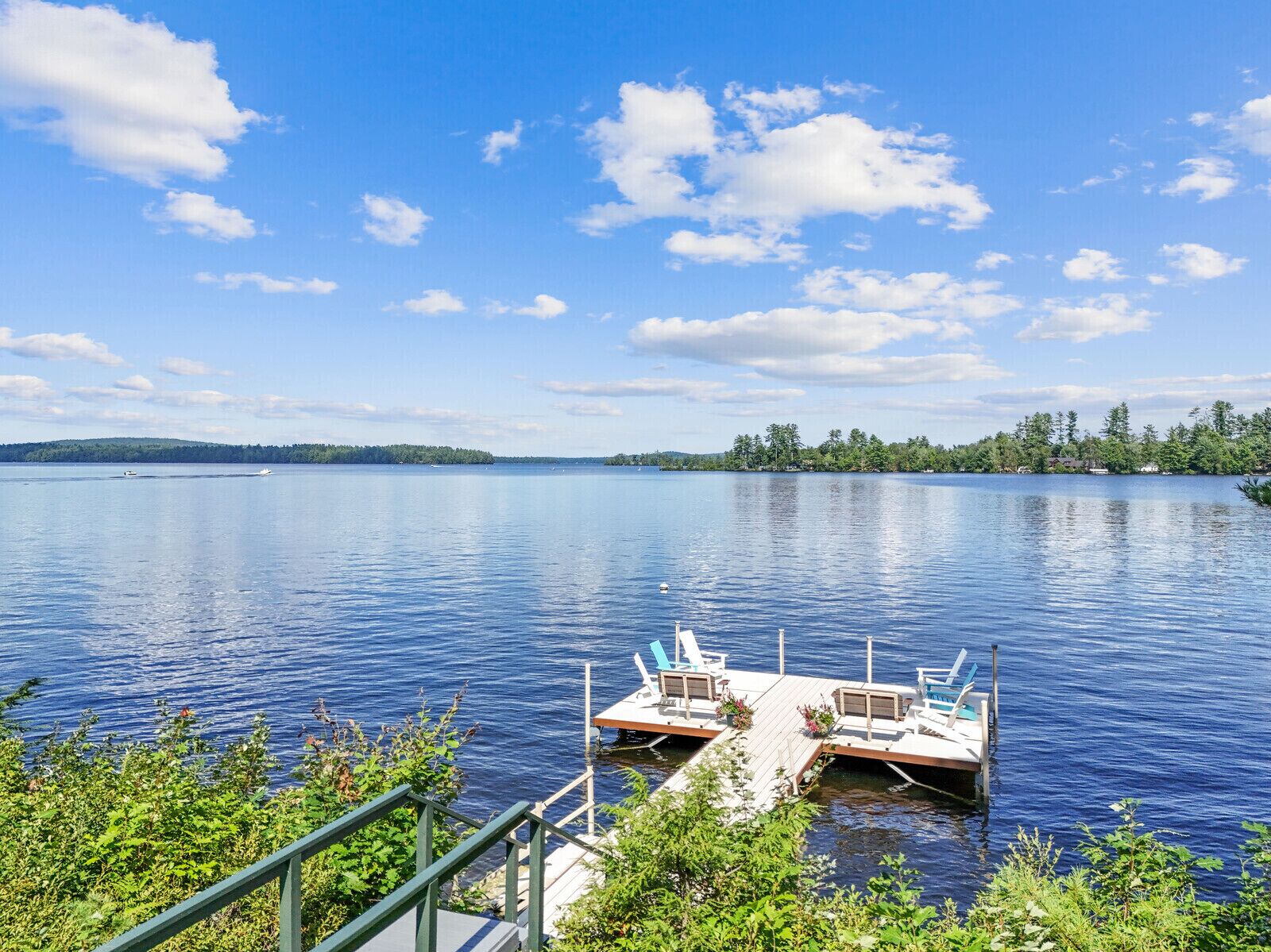 A dock with a small boat, surrounded by greenery and a calm lake under a clear sky.