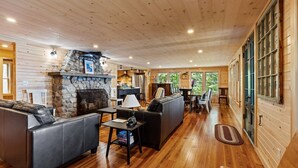 A cozy cabin interior with a stone fireplace, leather sofas, and a dining area.
