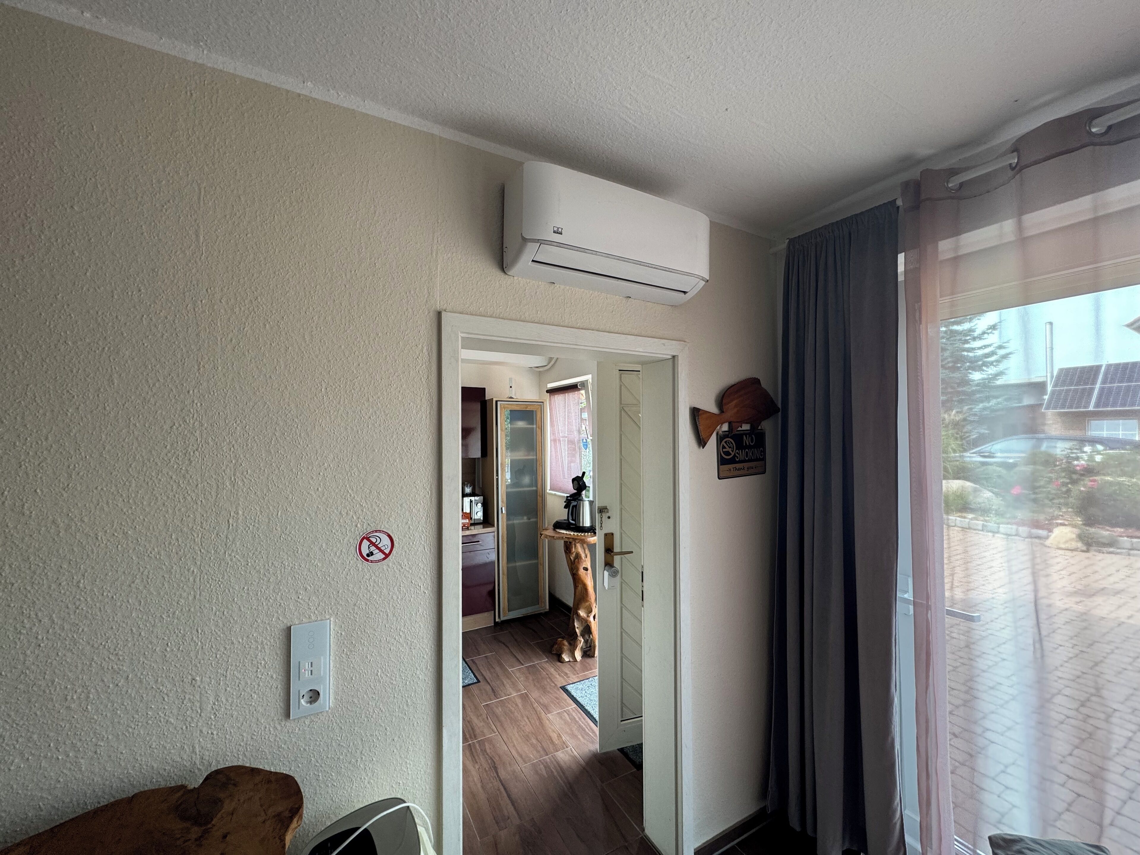 A room with a wooden floor, a dog, a no smoking sign, and a view of a building with solar panels.