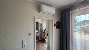 A room with a wooden floor, a dog, a no smoking sign, and a view of a building with solar panels.