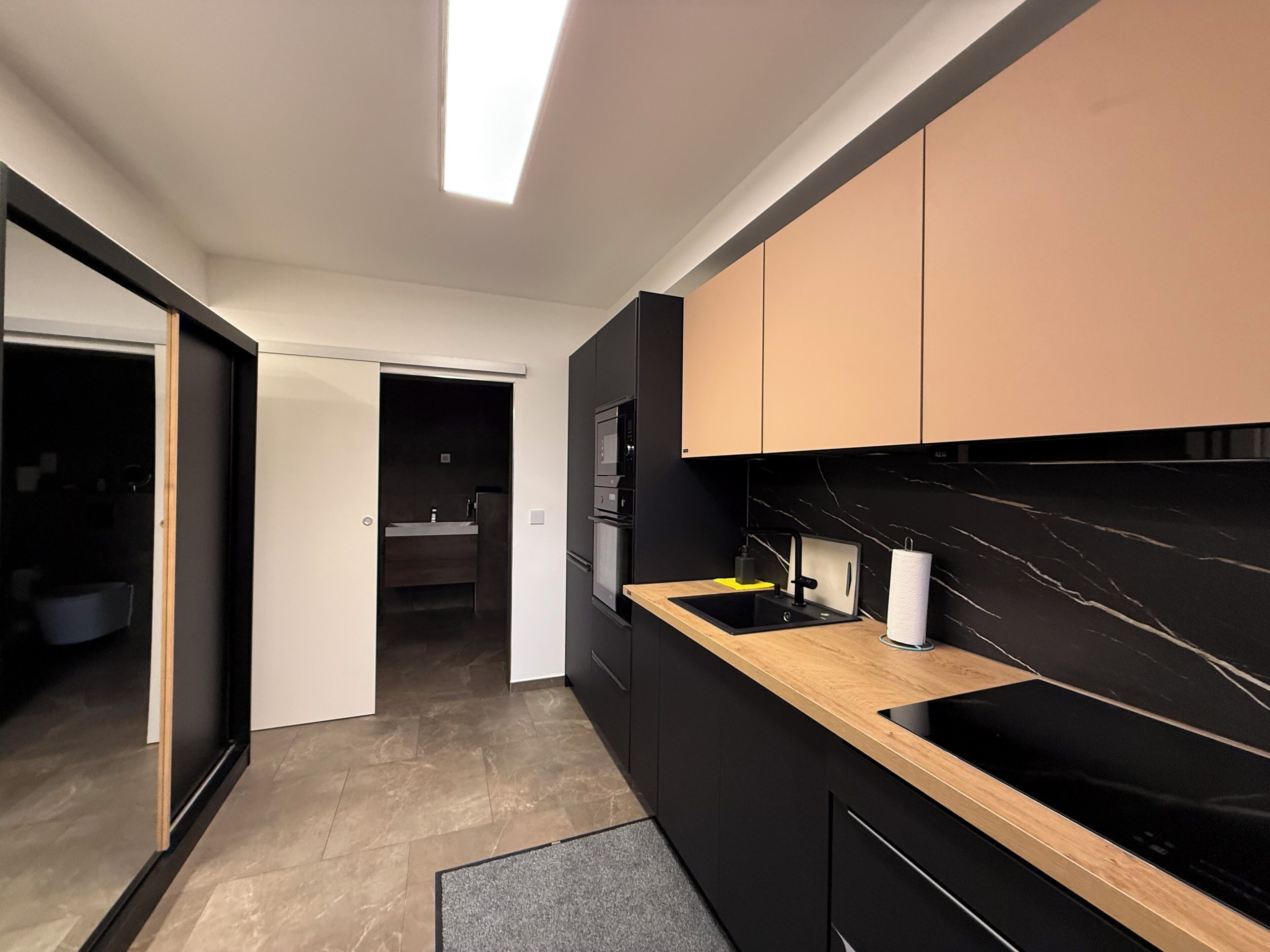 Een moderne keuken met zwarte en beige kastjes, een houten aanrecht en een zwarte achterwand.
