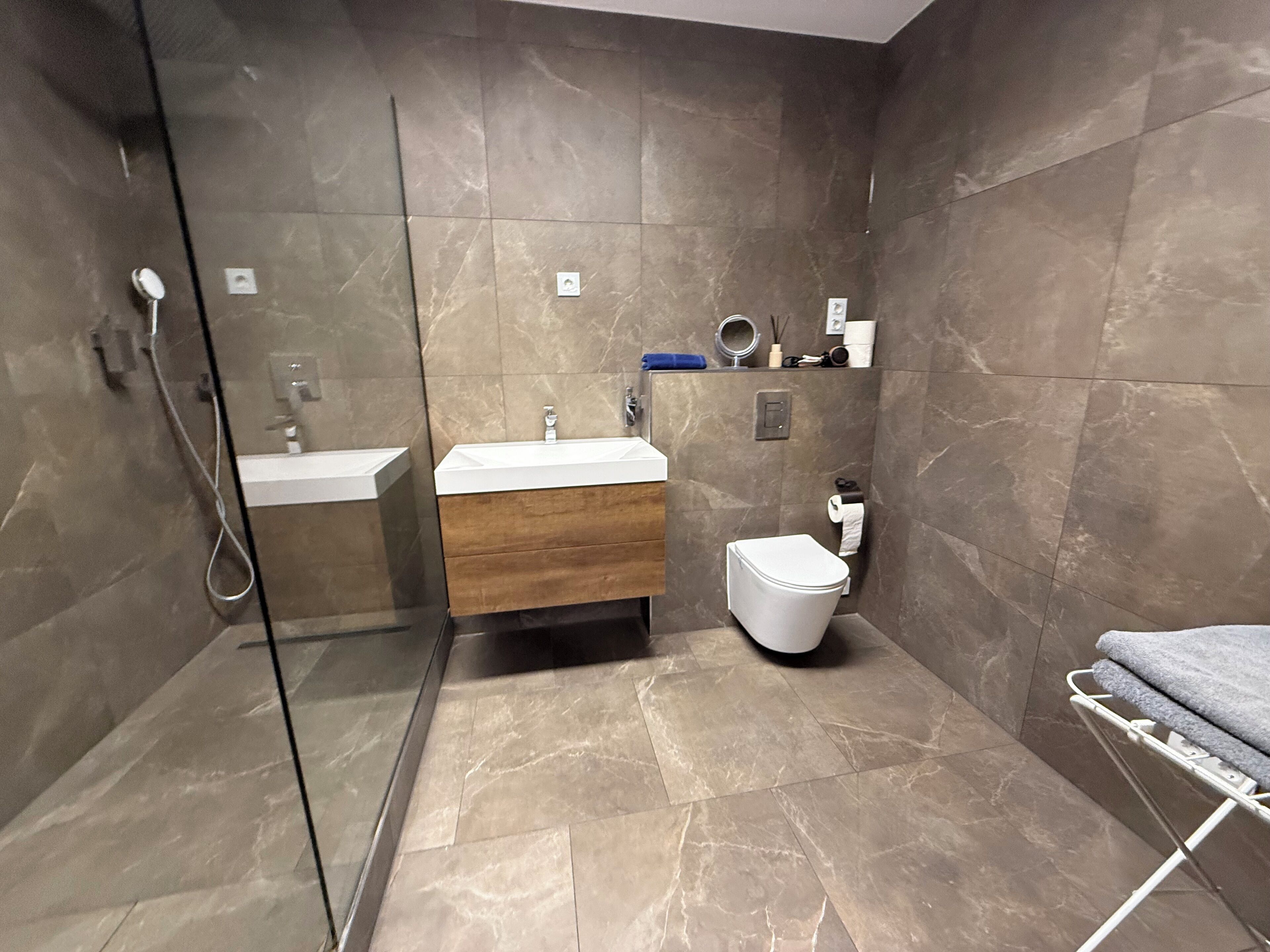 Un baño moderno con cabina de ducha de vidrio, tocador de madera, inodoro blanco y perchero para toallas.