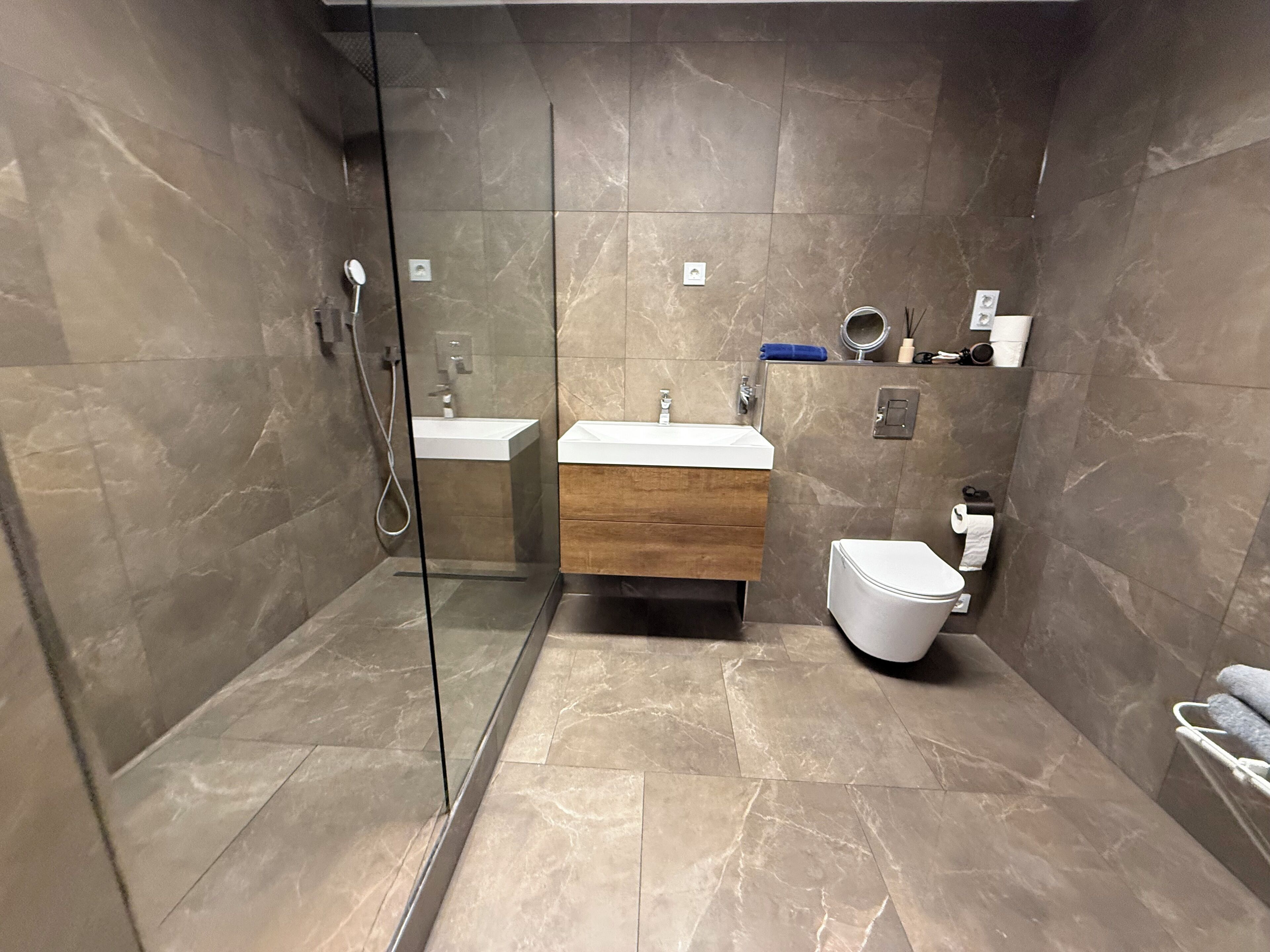 Une salle de bain moderne avec une douche à parois de verre, un meuble-lavabo en bois et des toilettes blanches.