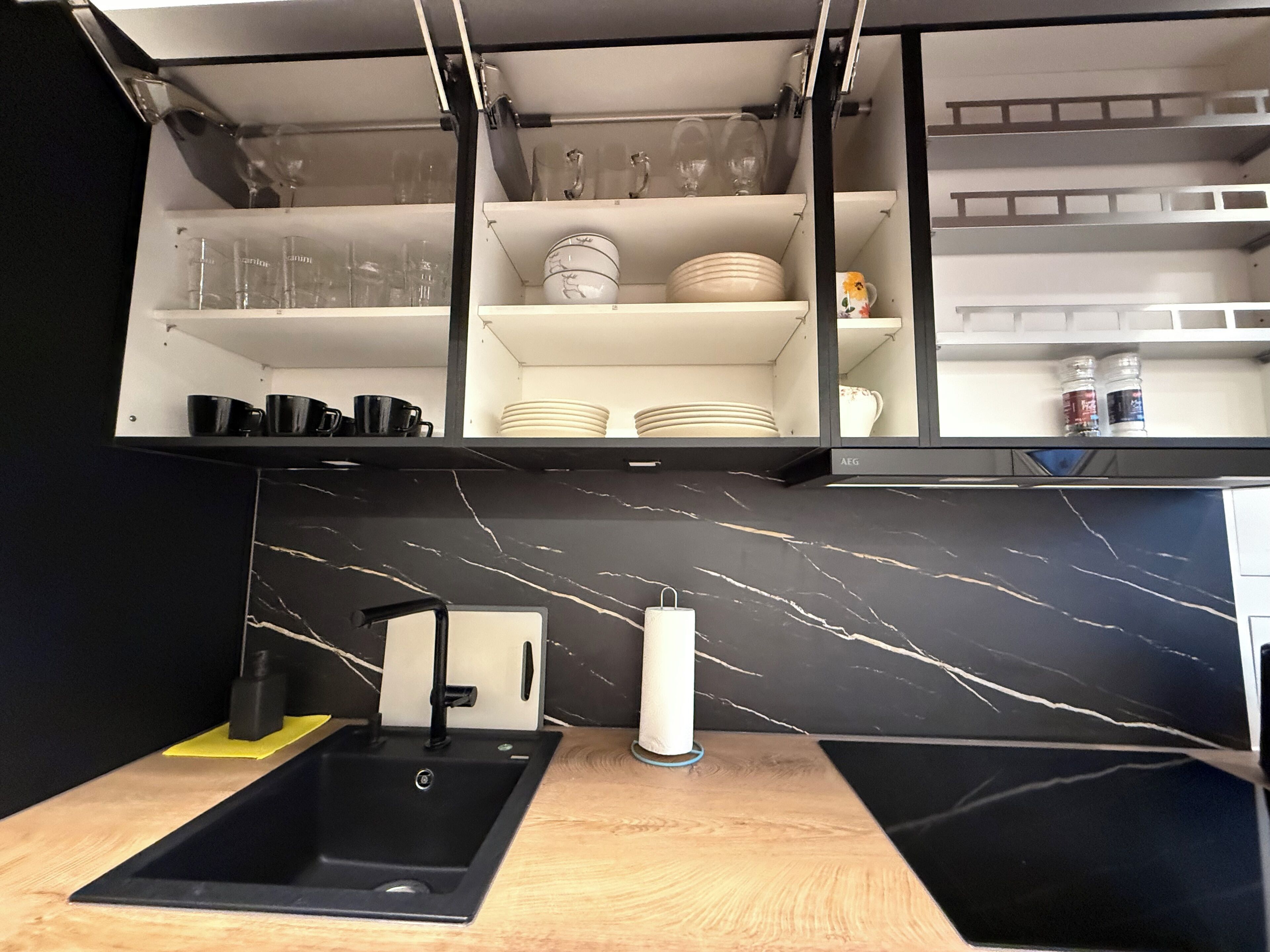 Een moderne keuken met zwarte aanrechtbladen, een zwarte spoelbak en een achterwand van marmer.