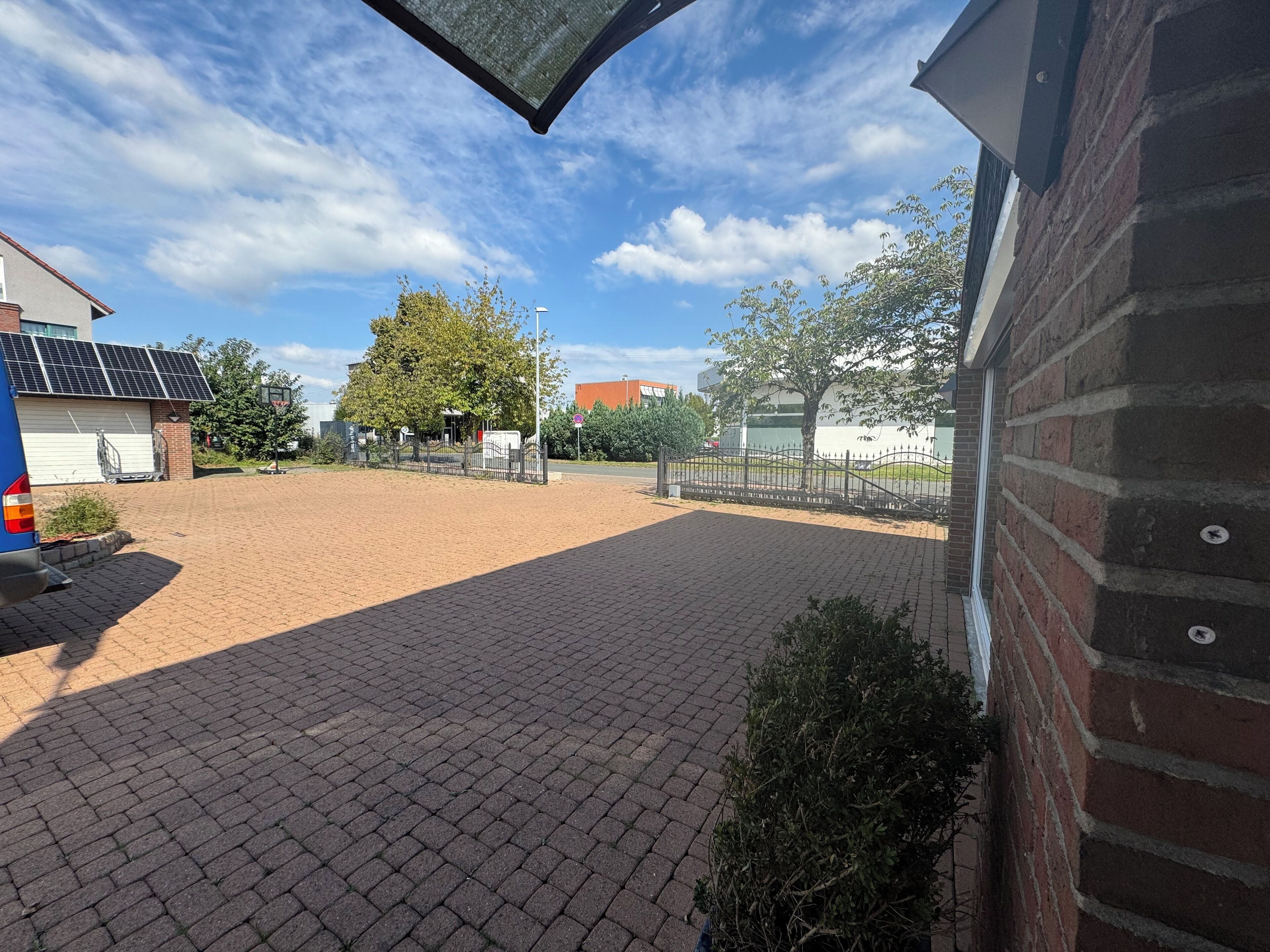 A paved courtyard with a brick building, a tree, and a fence.