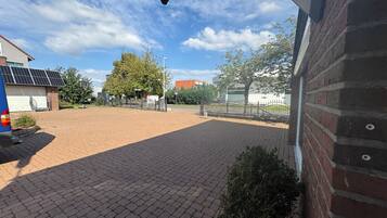 A paved courtyard with a brick building, a tree, and a fence.