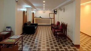 Un área de recepción con mostrador, asientos negros y rojos, piso estampado y luces en el techo.