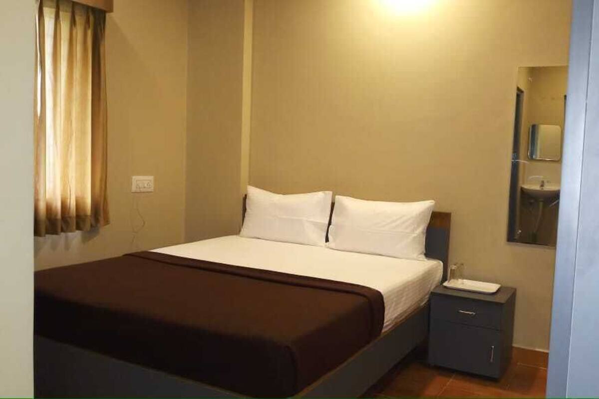 A single bed with white linens, a brown throw blanket, and a nightstand with a lamp.