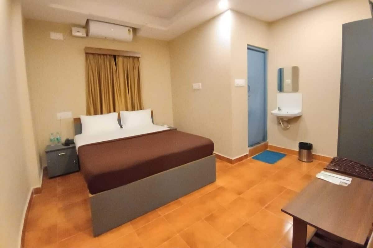 A hotel room with a bed, a desk, a chair, a small table, a nightstand, a mirror, a door, and a window with curtains.