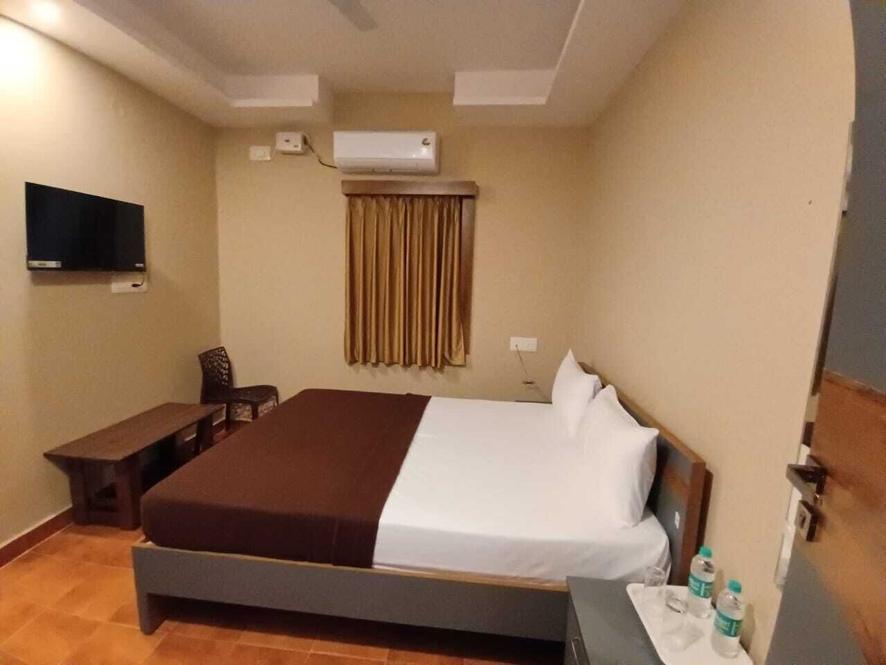 A hotel room with a bed, a desk, a chair, a television, and an air conditioning unit.