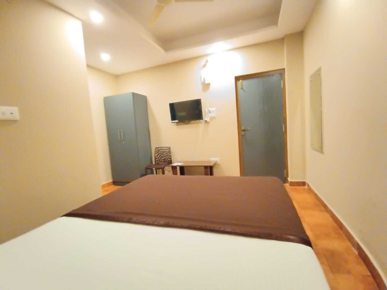 A bedroom with a bed, a TV mounted on the wall, a wardrobe, and a door.