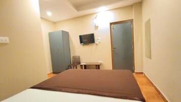 A bedroom with a bed, a TV mounted on the wall, a wardrobe, and a door.