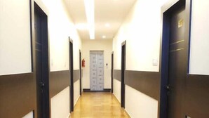 Un pasillo largo y estrecho con suelo de baldosas, flanqueado por puertas a ambos lados.