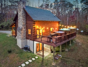 A log cabin with a stone chimney, a deck with outdoor seating, and a hot tub. - The Hidden Gem | Hocking Hills, Log Cabin, Hot Tub (Logan)