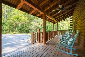 A wooden porch with rocking chairs and a view of a forested area. - The Hidden Gem | Hocking Hills, Log Cabin, Hot Tub (Logan)