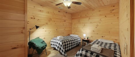 A wooden cabin with two beds, a ceiling fan, a lamp, and a small table with a lamp.