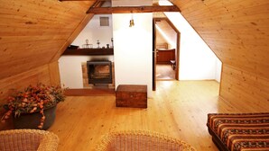 Acogedor dormitorio en el desván con paredes de madera y techo inclinado, que incluye una chimenea, un cofre de madera y muebles de mimbre.