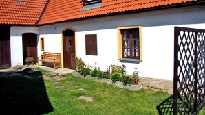 Una casa tradicional con techo de tejas rojas, un banco de madera y un jardín con flores de colores.