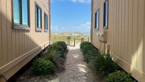 A pathway between two buildings with a clear sky and distant dunes.