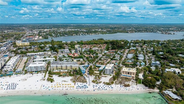 An aerial view of a coastal town with a beach, hotel buildings, and a marina.
