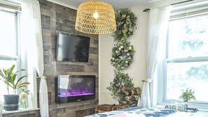 Een slaapkamer met een groot bed, een flatscreen televisie aan de muur, een houten accentmuur, een hangende lamp en een raam met gordijnen.